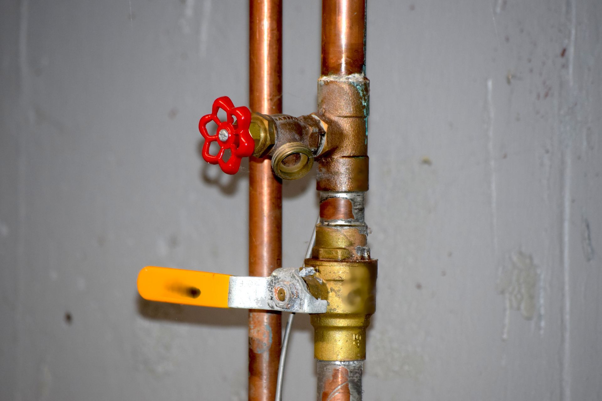 Copper pipes with red and yellow handled valves against a gray wall.
