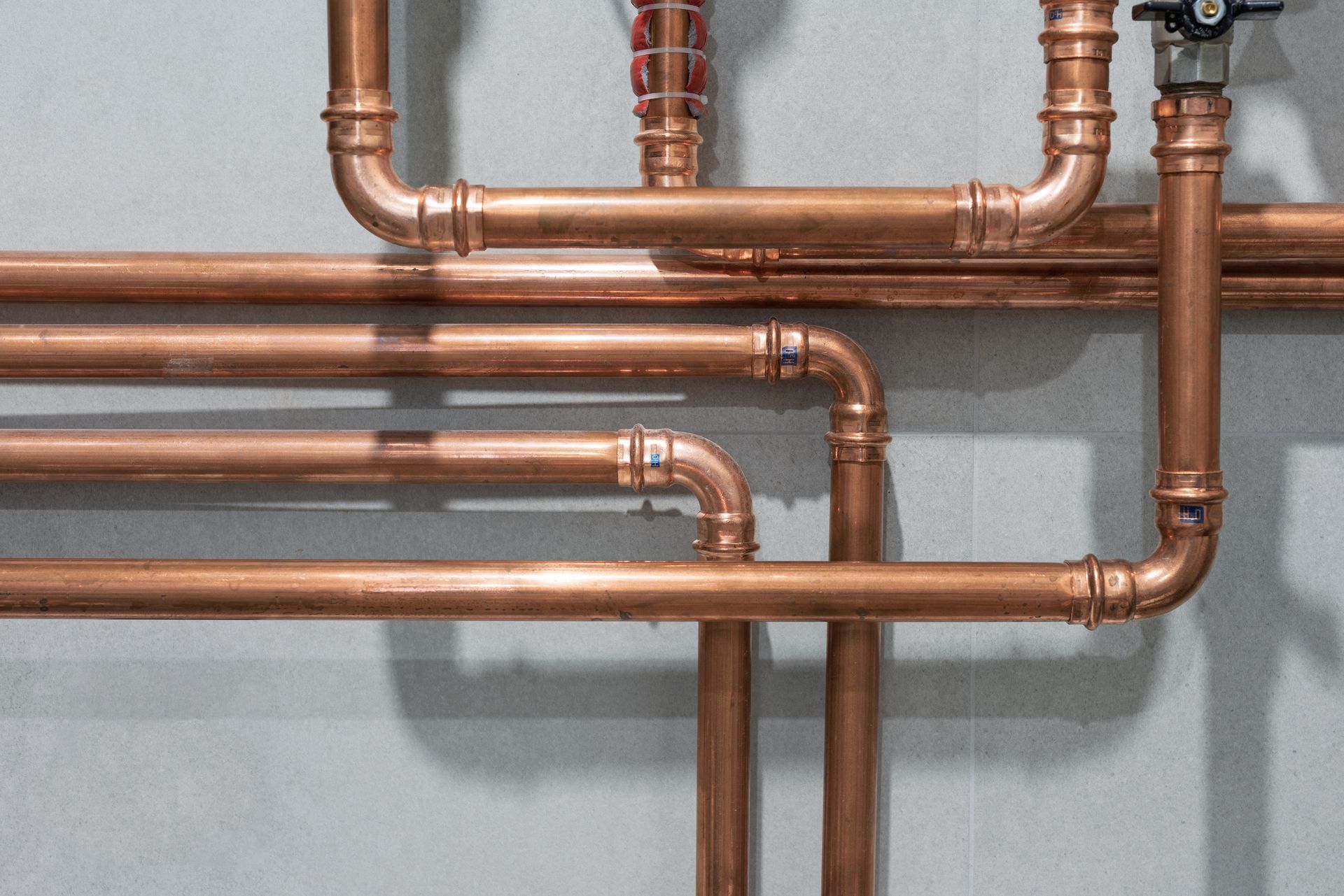 Copper pipes and fittings on a gray wall, forming a plumbing system.