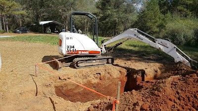 Mini excavator digging a trench in dirt, outdoors.