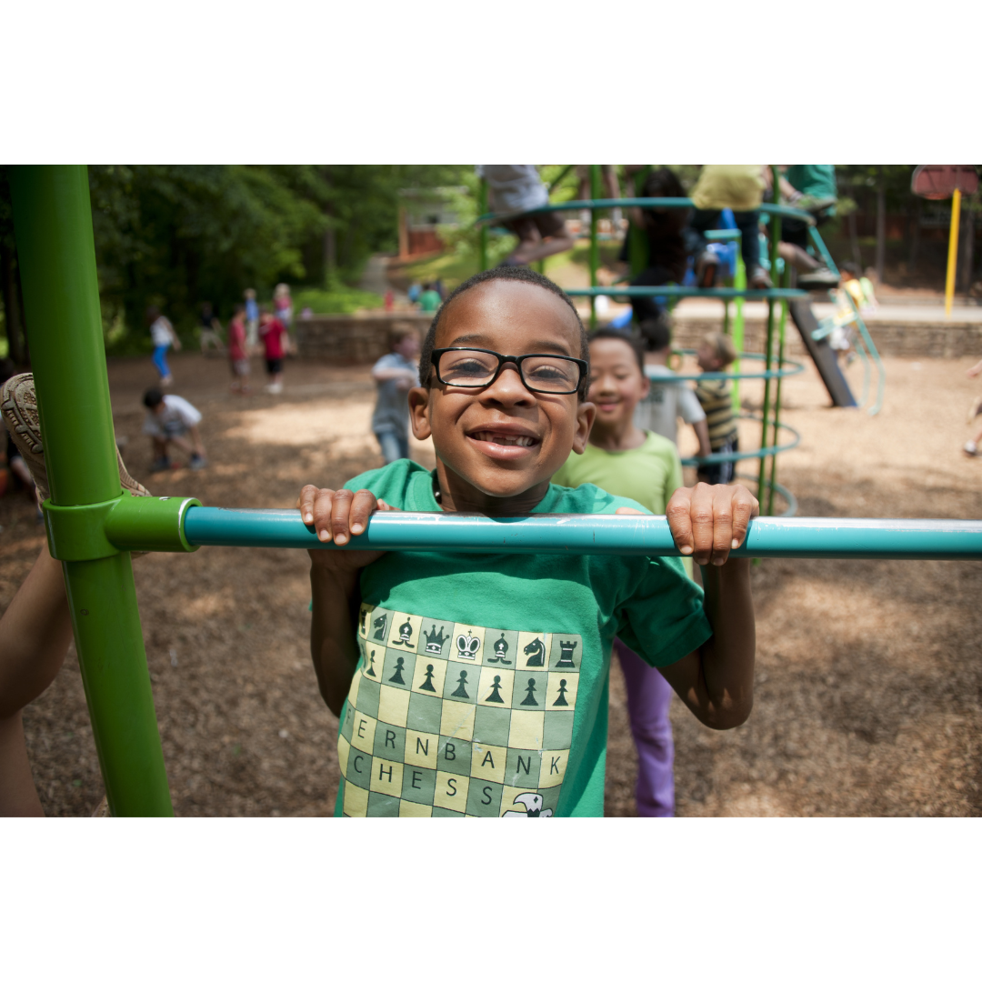 A young boy wearing glasses is hanging from a bar at a playground.