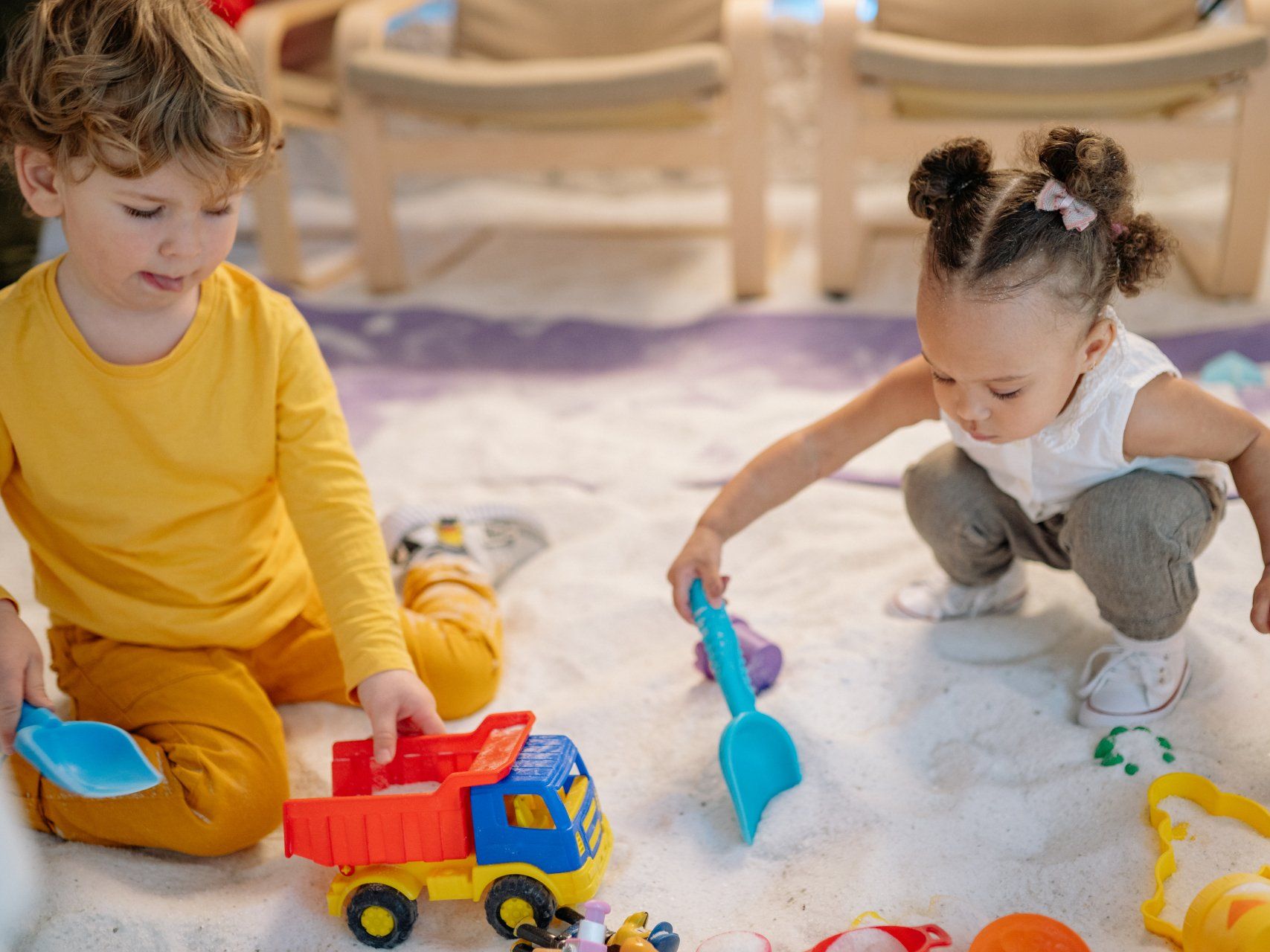 A boy and a girl are playing in the sand with toys.