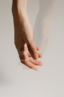 Mano sfocata in movimento, che si abbassa con le dita leggermente estese su uno sfondo bianco.