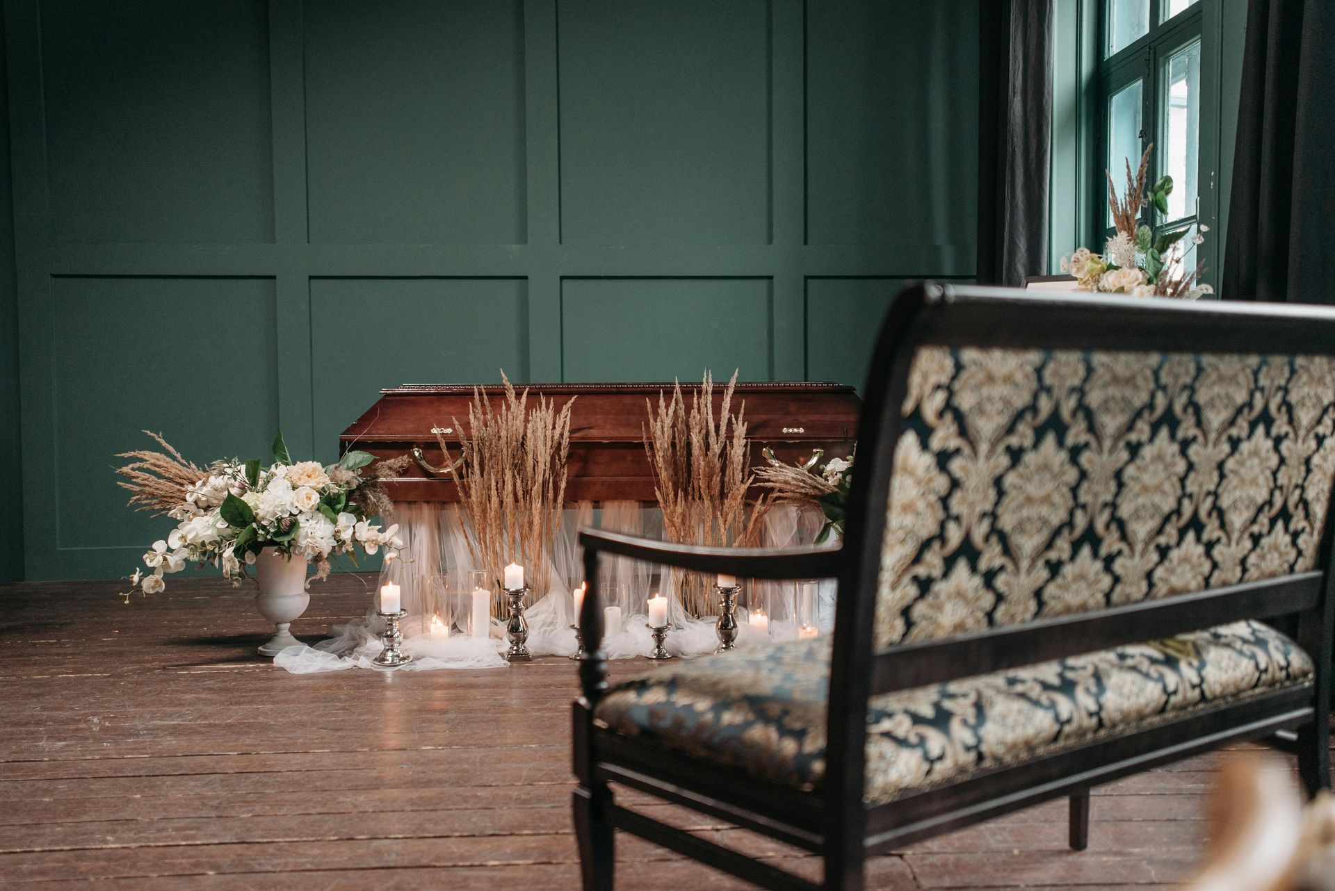 Una bara decorata con fiori e candele; una panca decorativa di fronte. Pareti verdi, pavimento in legno.