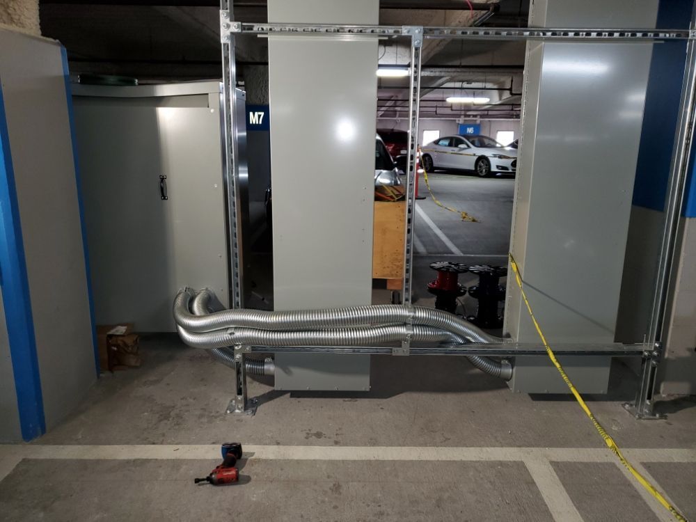 A car is parked in a parking garage next to a wall with pipes coming out of it.