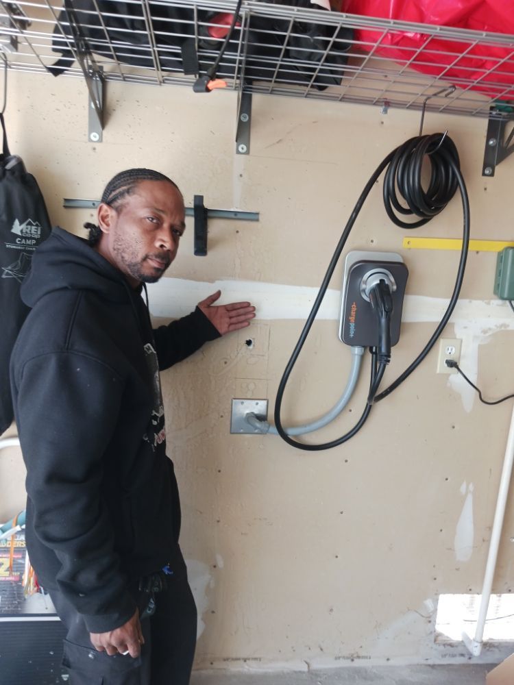 A man in a black hoodie is standing in a garage next to a charger