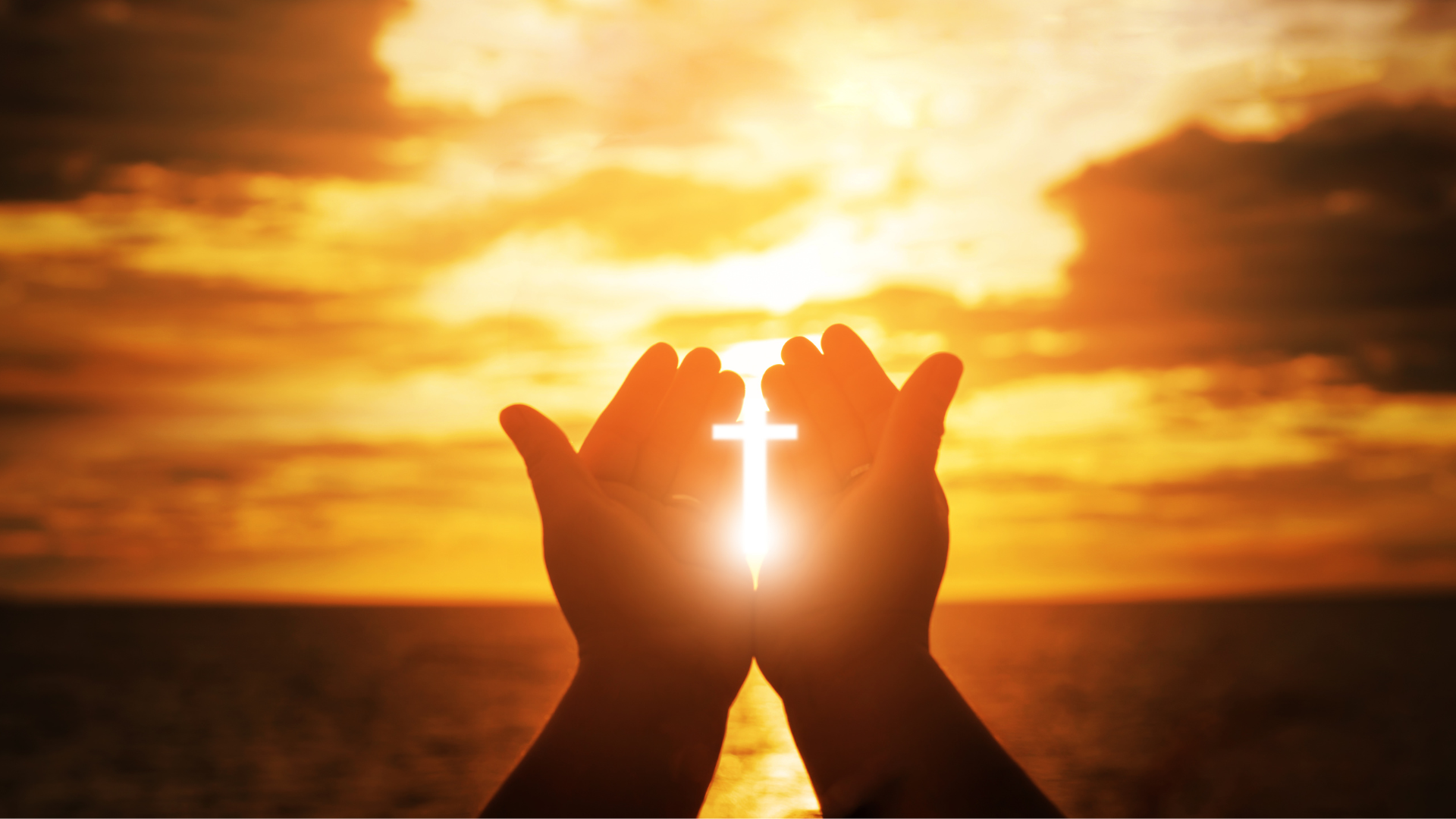 A person is holding a cross in their hands in front of a sunset.