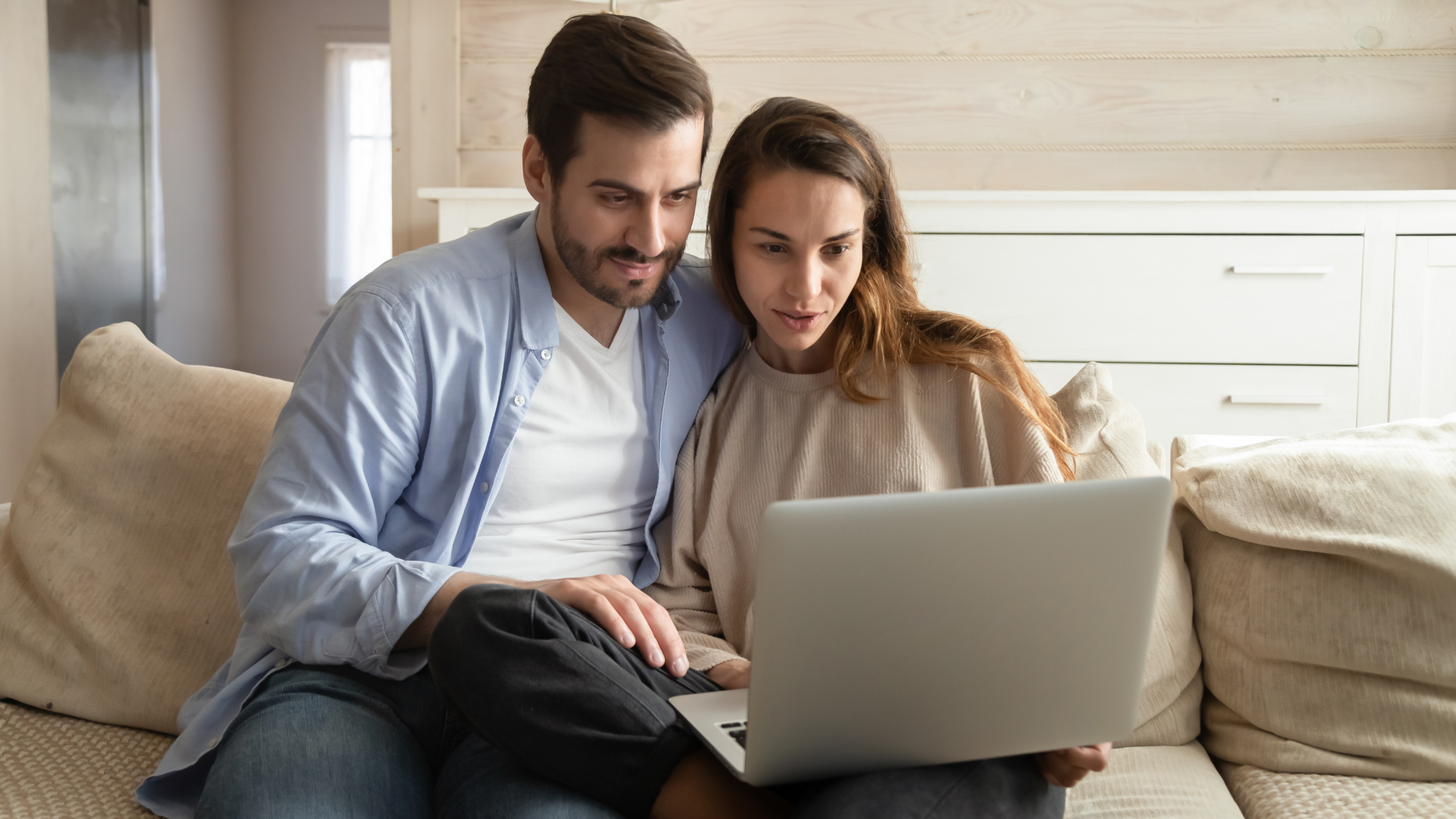 A man and a woman are sitting on a couch looking at a laptop.