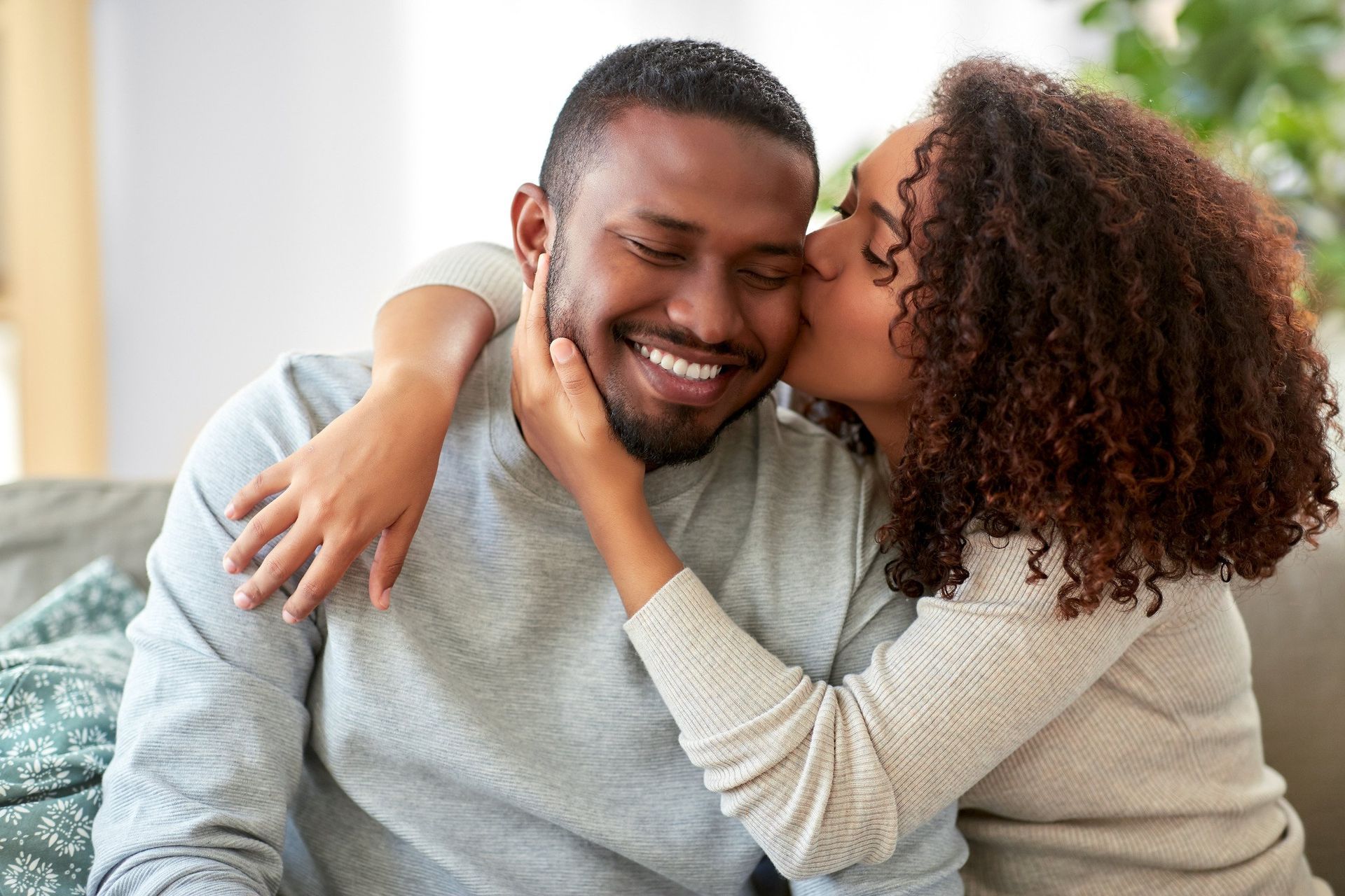 A woman is kissing a man on the cheek while they are sitting on a couch.