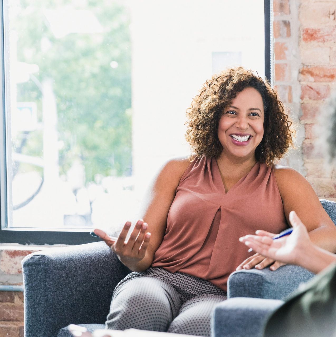 A woman is smiling while sitting in a chair in front of a window.