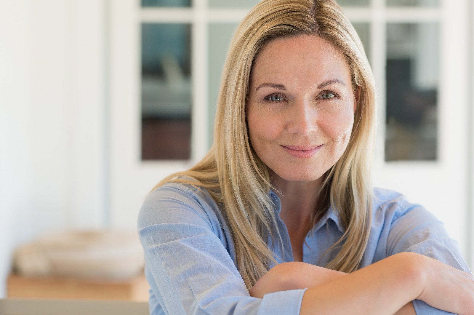 A woman is sitting with her arms crossed and smiling at the camera.