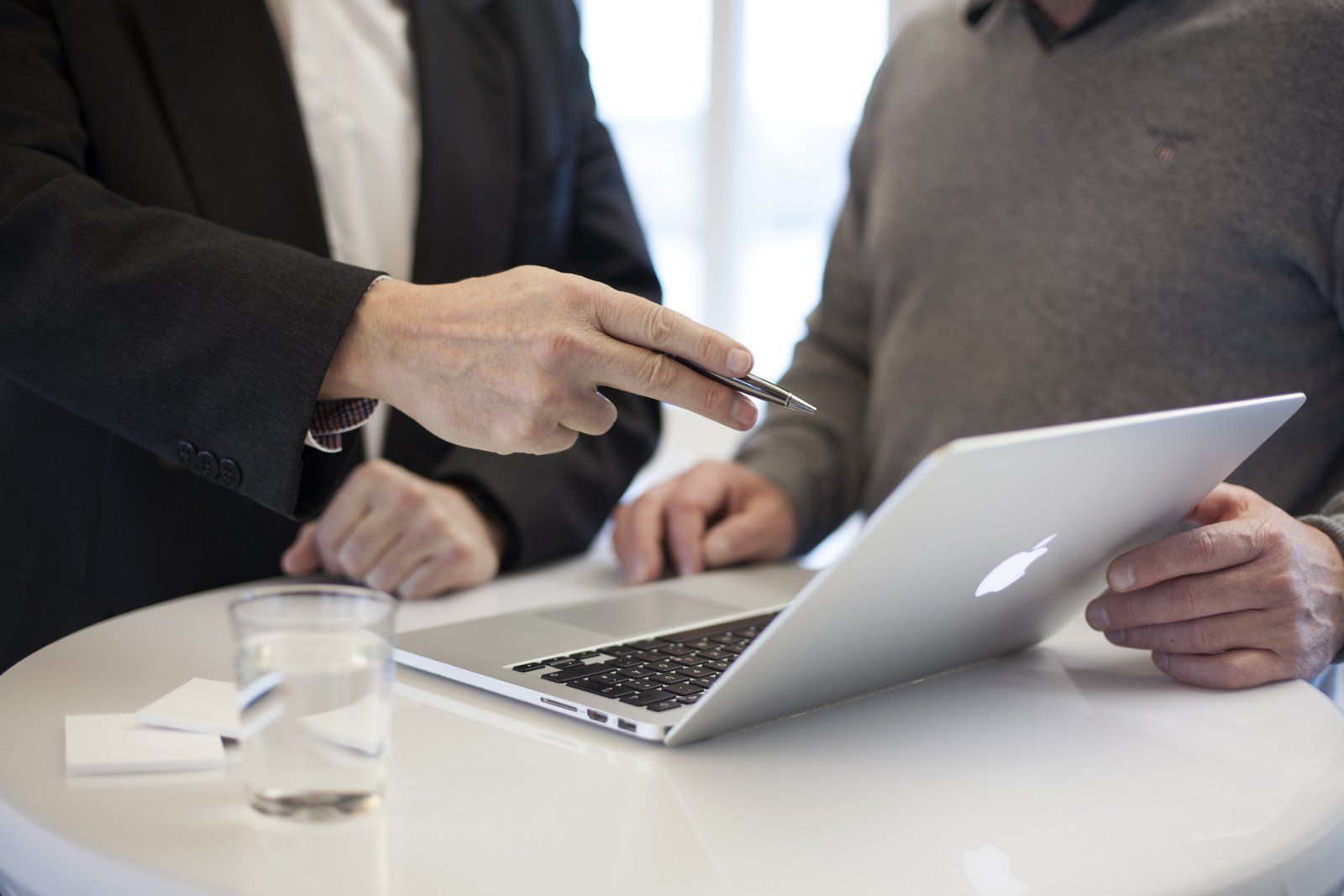Two men are sitting at a table looking at a laptop computer.