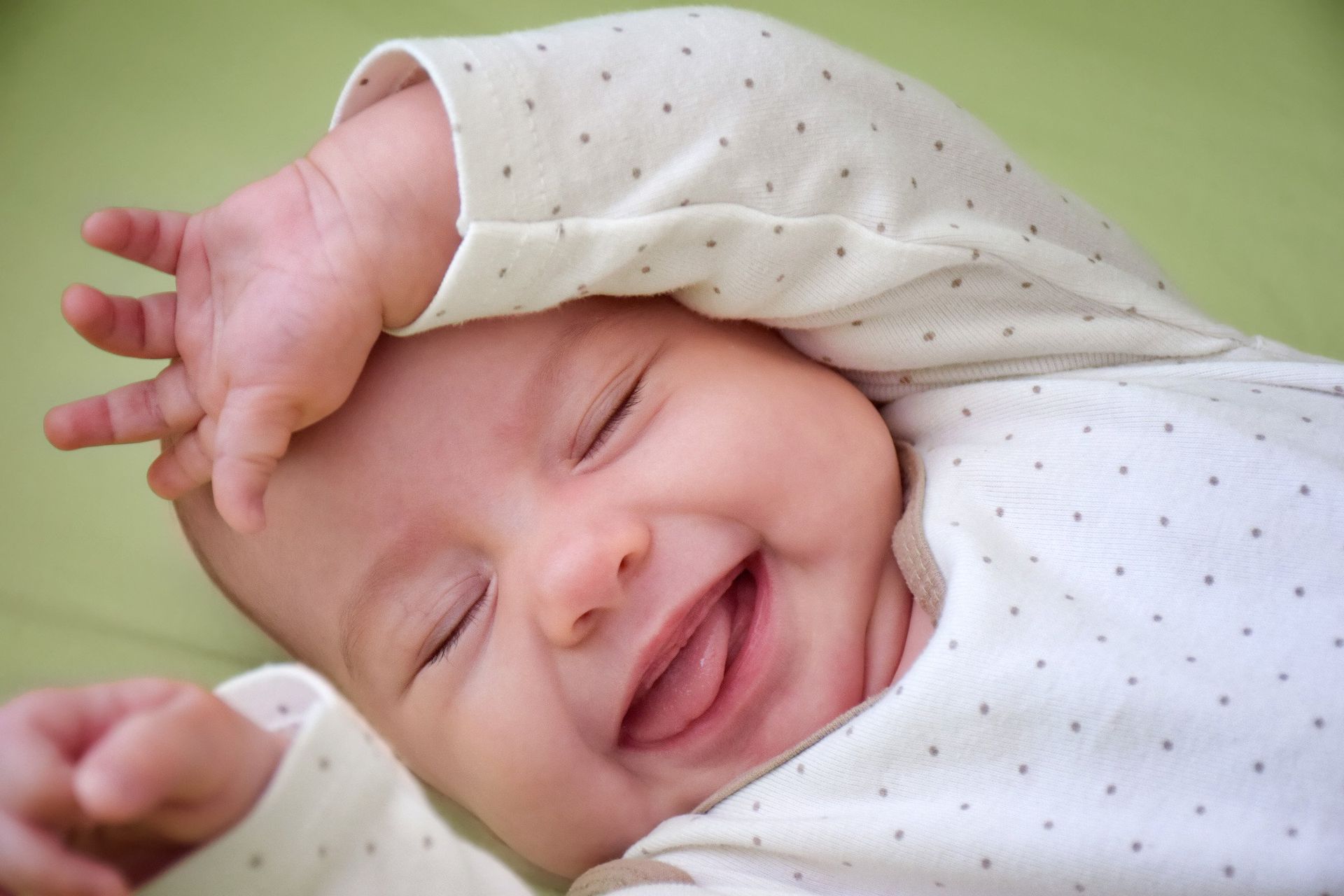 A baby is smiling while laying on a green blanket.