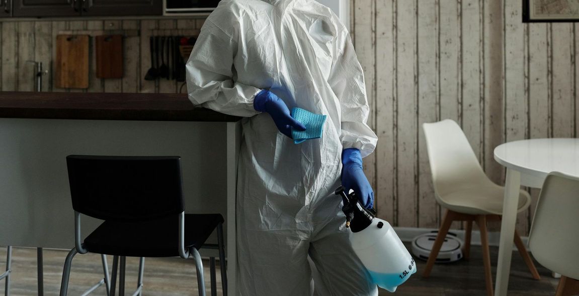 A person in a protective suit is disinfecting a room with a spray bottle.