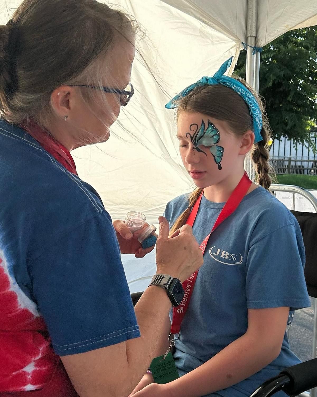 A woman is painting a butterfly on a young girl 's face.