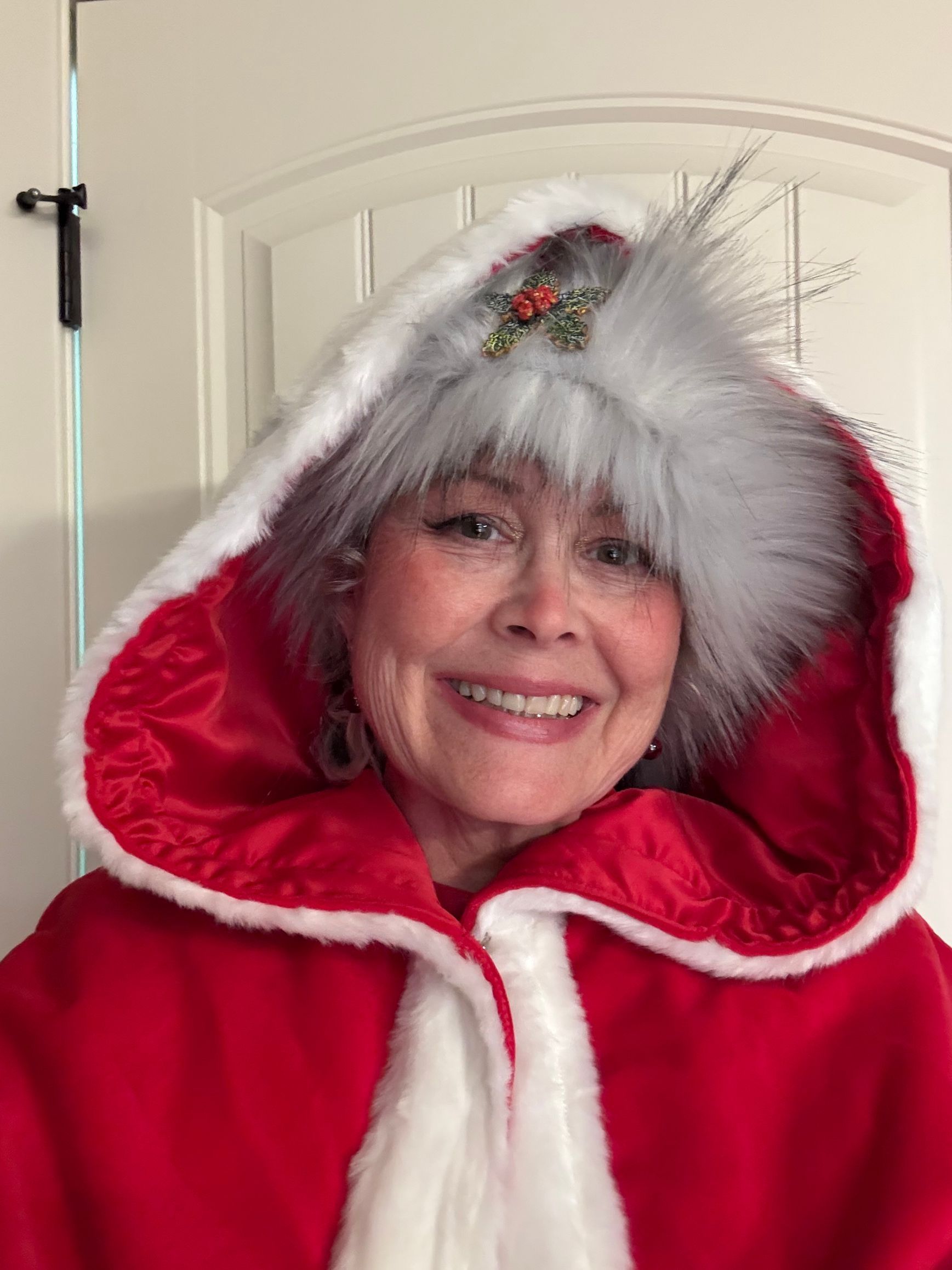 Woman in red and white Christmas cape with hood, smiling.