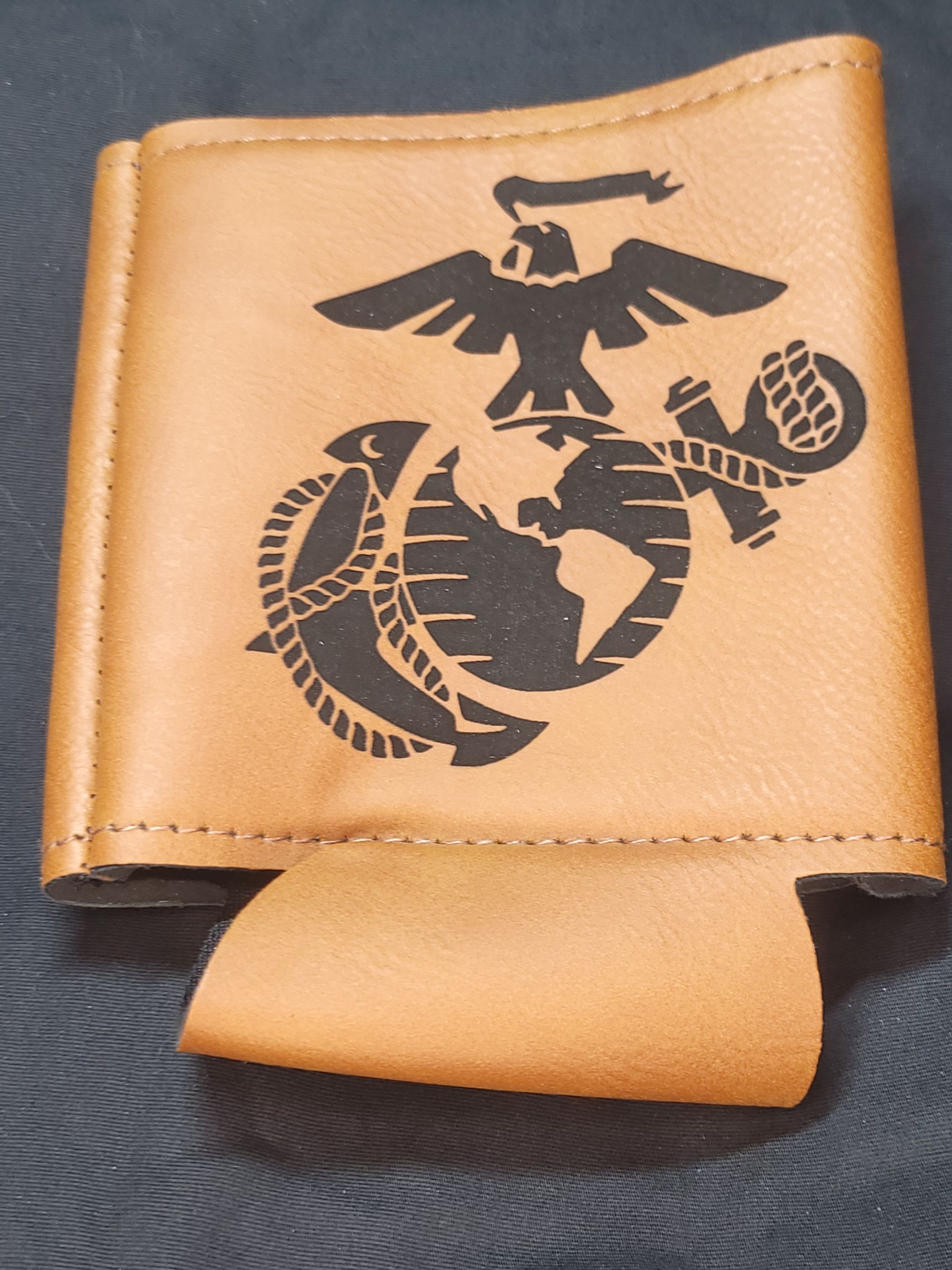 A brown leather can holder with a marine logo on it