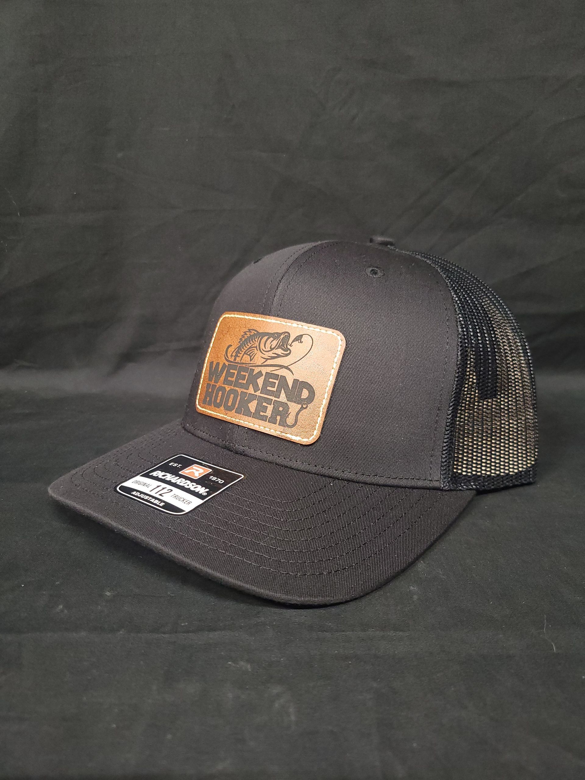A black trucker hat with a brown leather patch is sitting on a black surface.