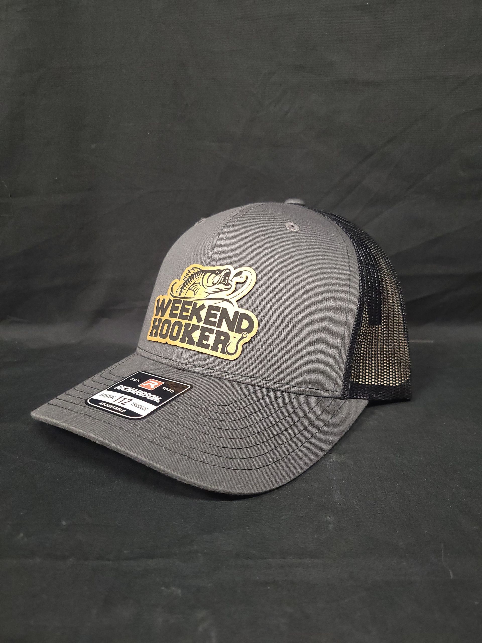 A gray trucker hat with a gold logo on it is sitting on a black surface.