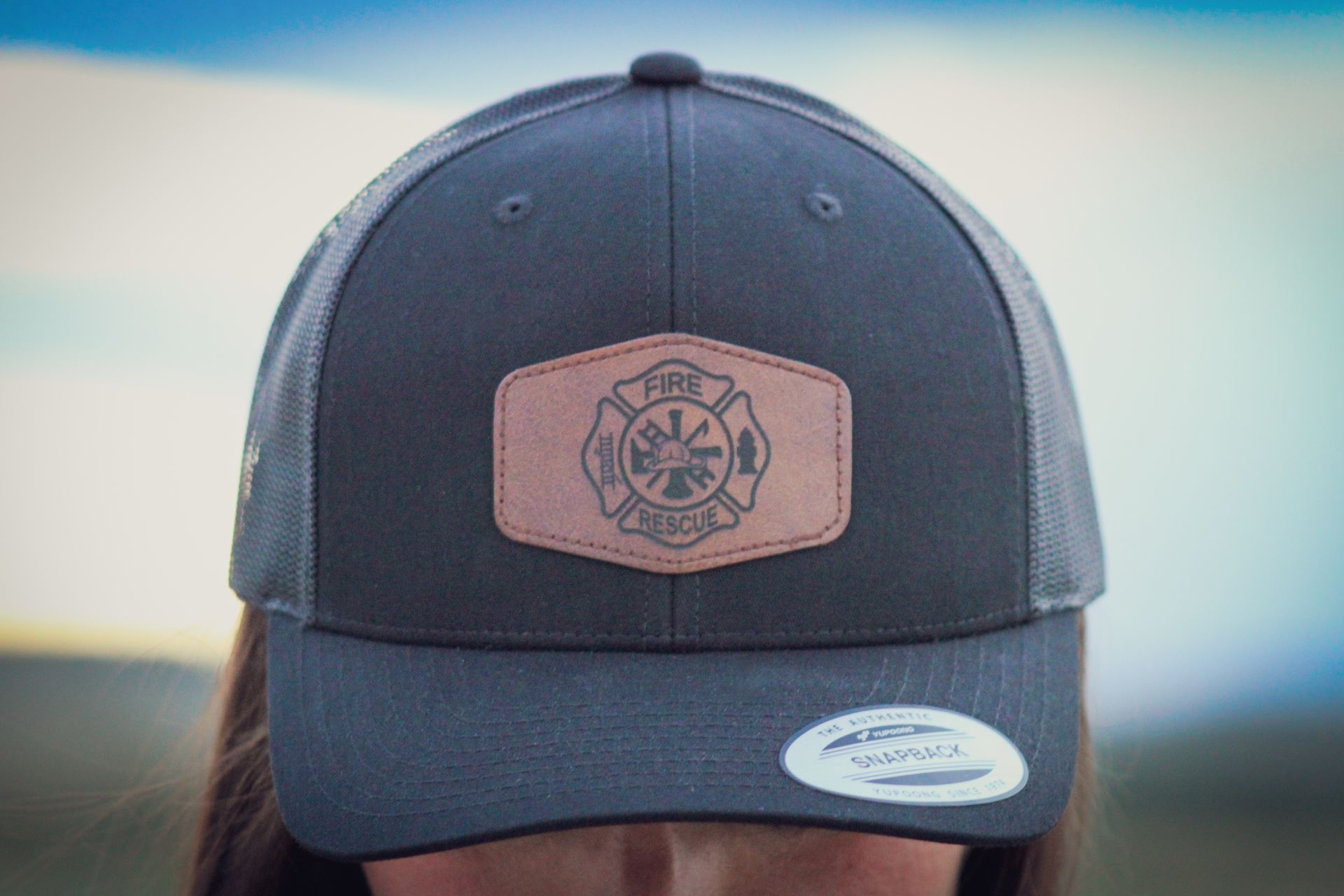 A woman is wearing a baseball cap with a leather patch on it.