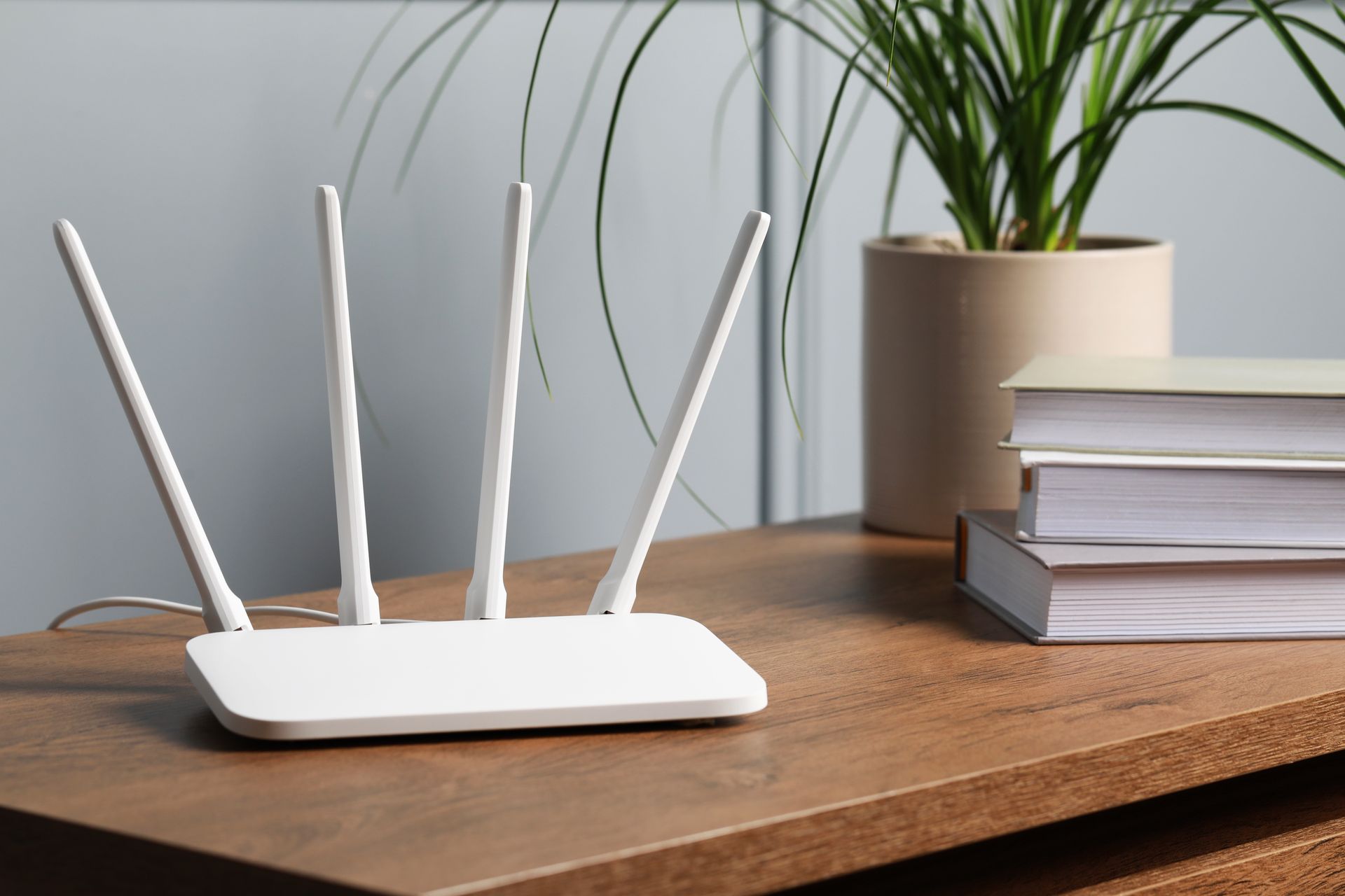 A white router is sitting on a wooden table next to books and a potted plant.