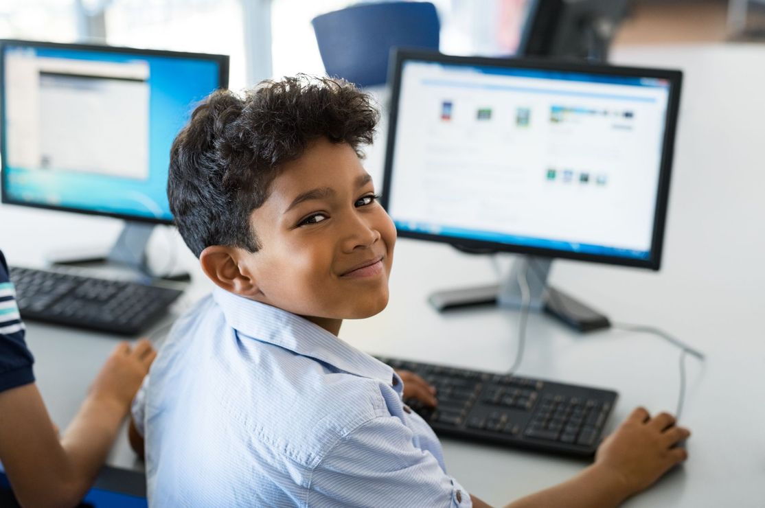 A young boy is sitting at a desk in front of a computer.