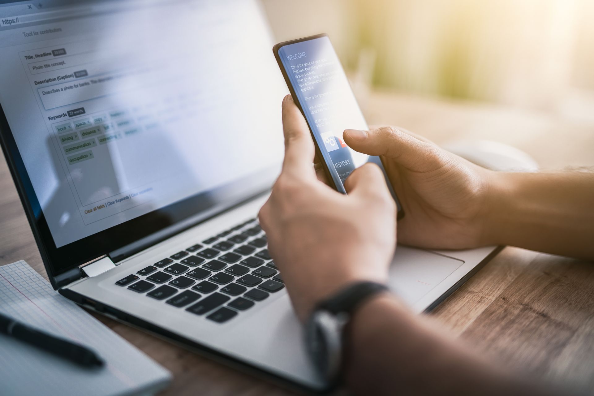 A person is using a cell phone in front of a laptop computer.