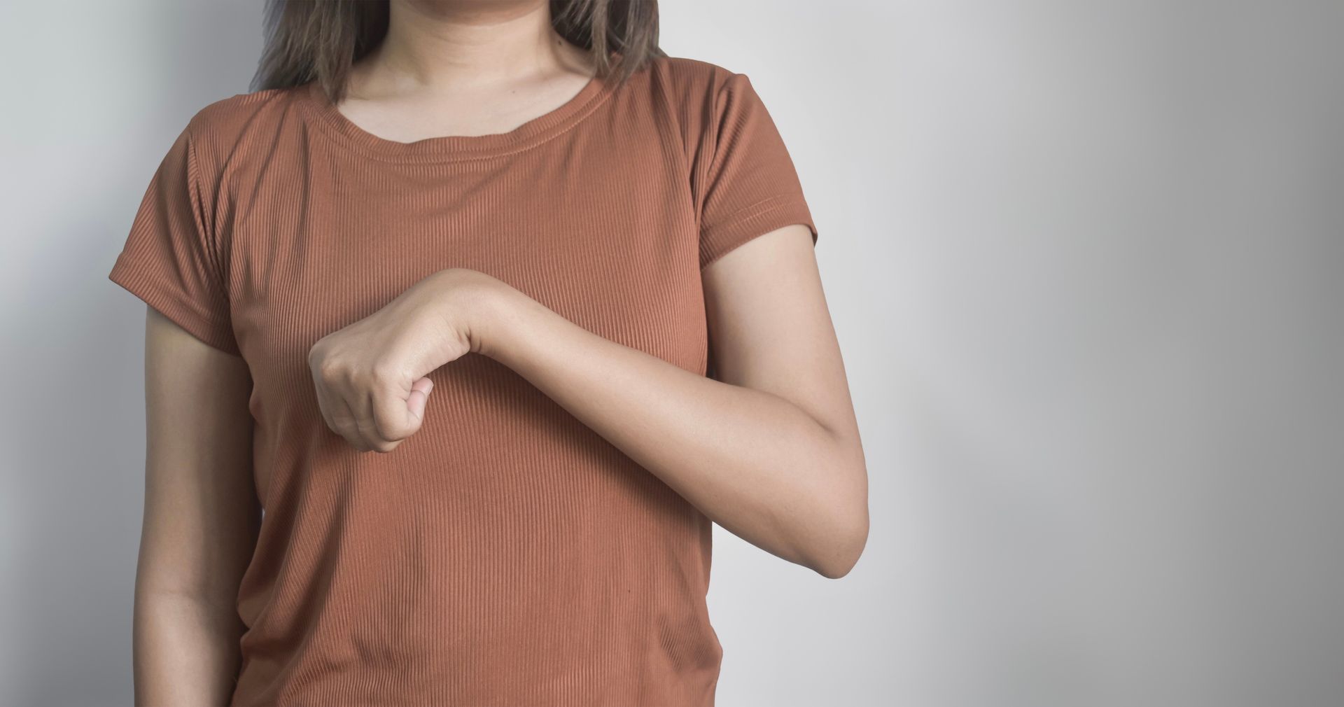 Pessoa vestindo camisa marrom, fechando o punho e apontando-o em direção ao peito.