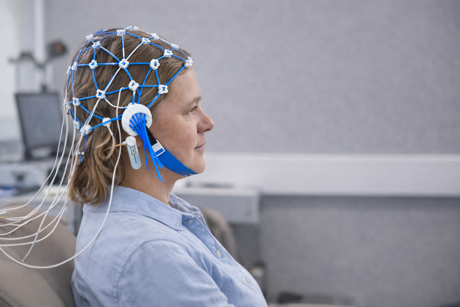 Mulher usando touca de EEG para monitoramento de ondas cerebrais, em um ambiente médico.