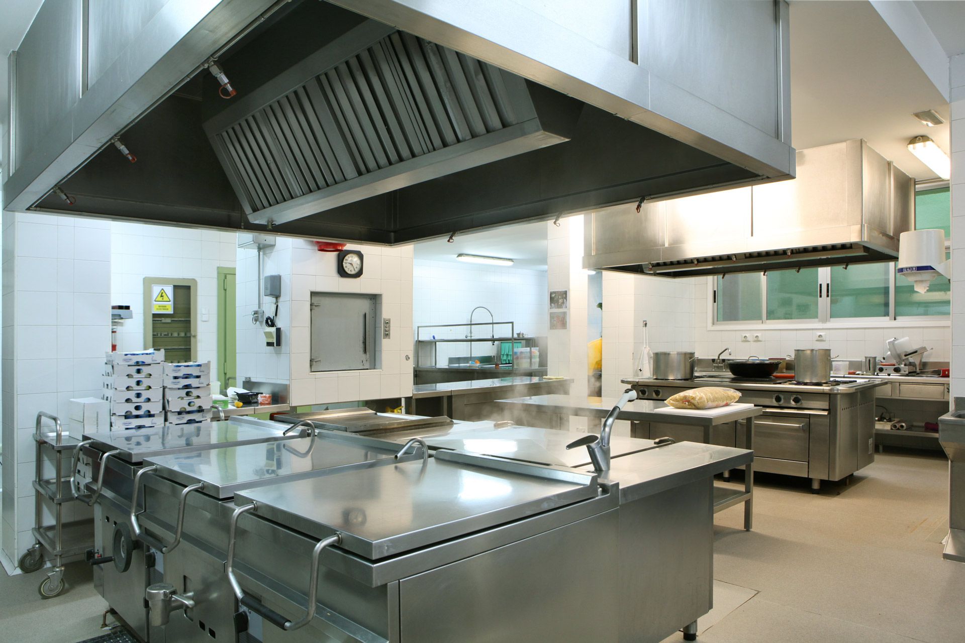 Commercial kitchen with stainless steel equipment and ventilation hoods.