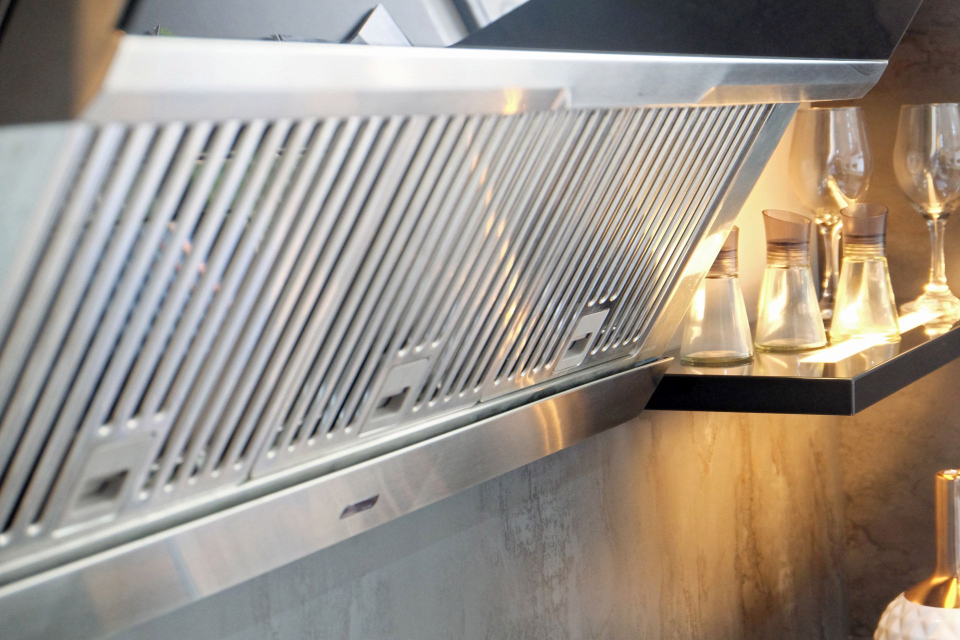 Stainless steel kitchen range hood with a shelf holding salt and pepper shakers.