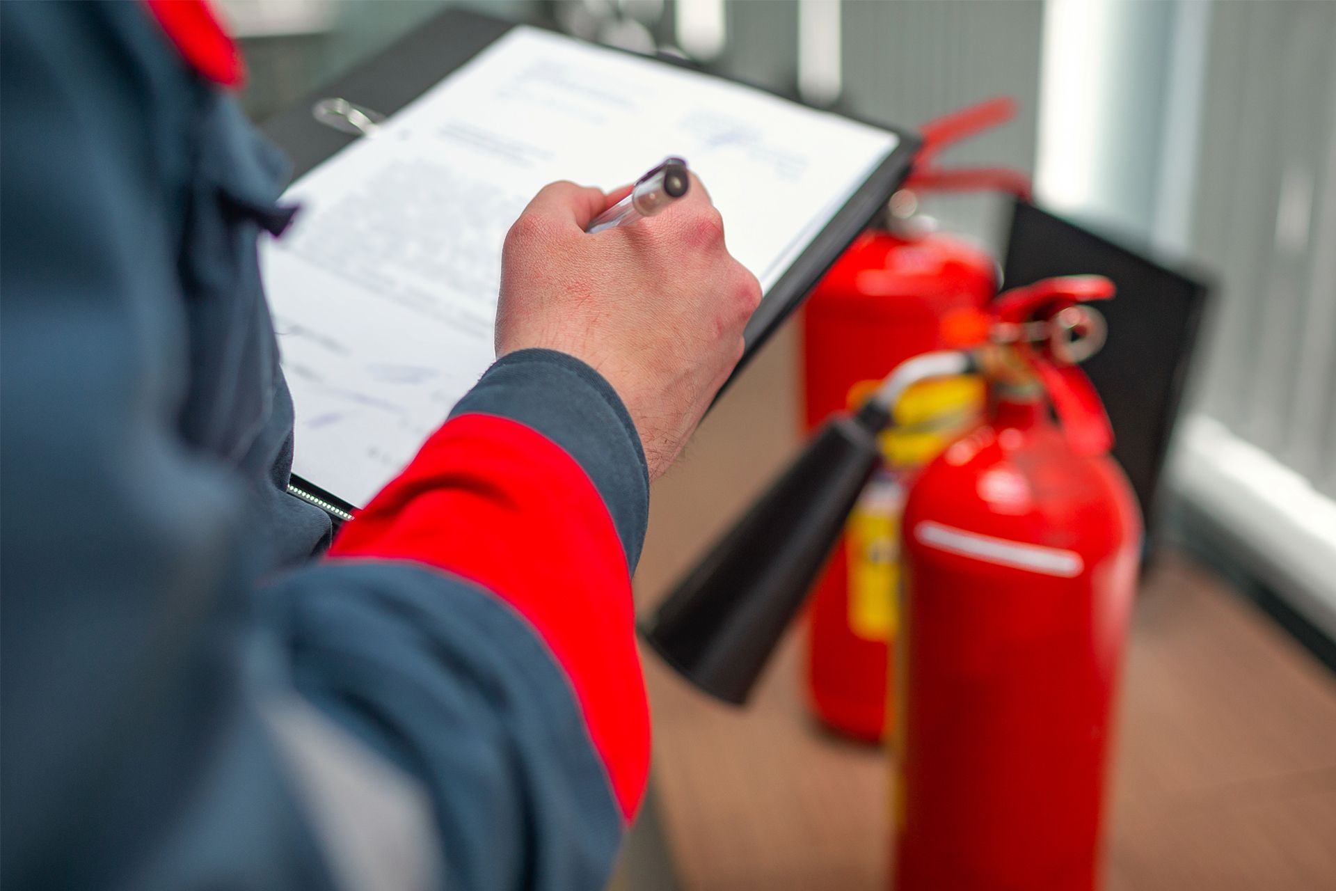 Person in uniform inspecting fire extinguishers, writing on a clipboard.