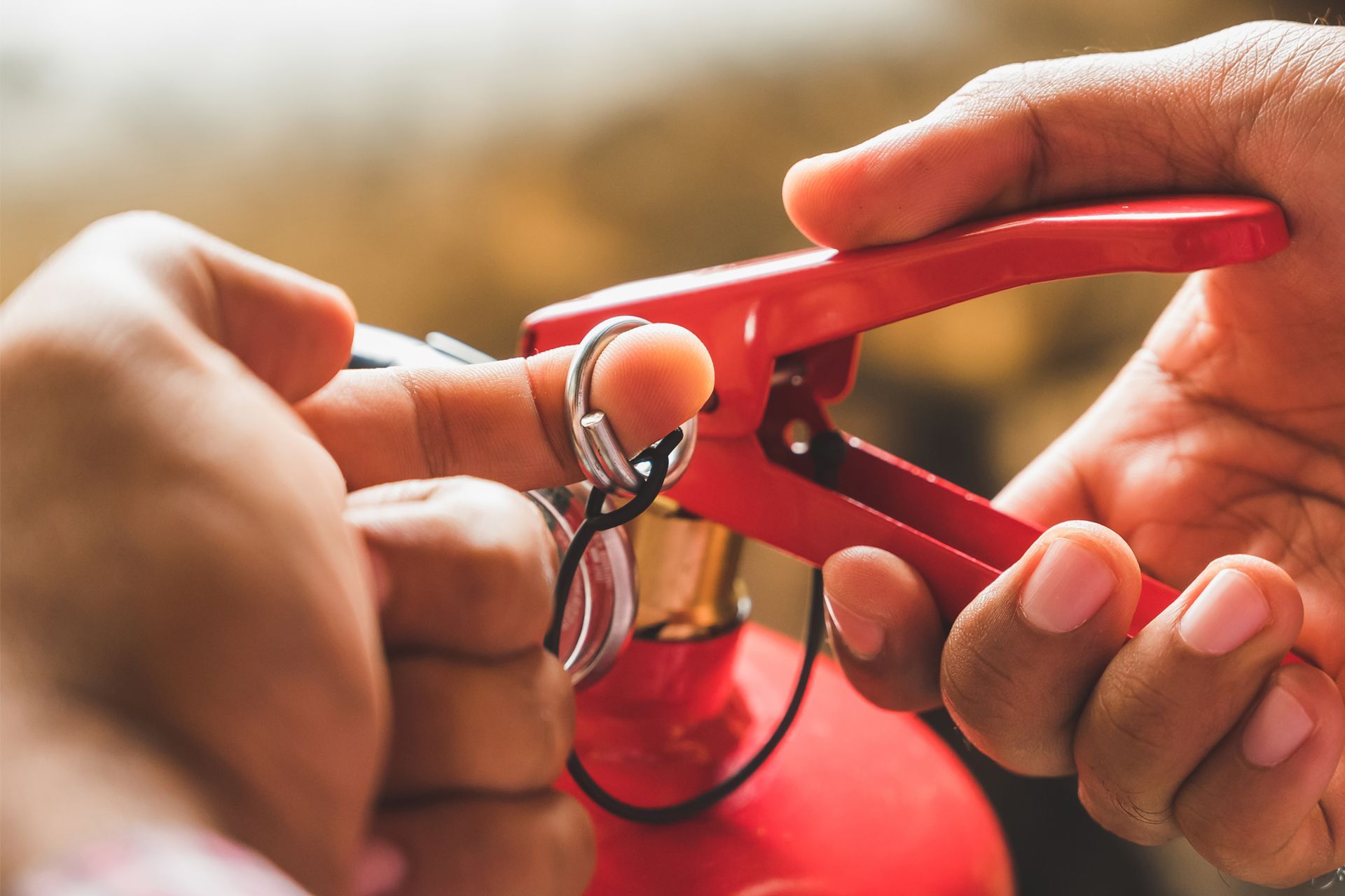 Person's hands removing safety pin from a red fire extinguisher handle.