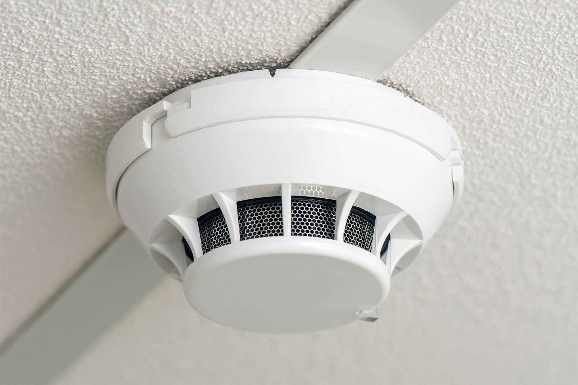 White smoke detector mounted on a white ceiling, angled view.