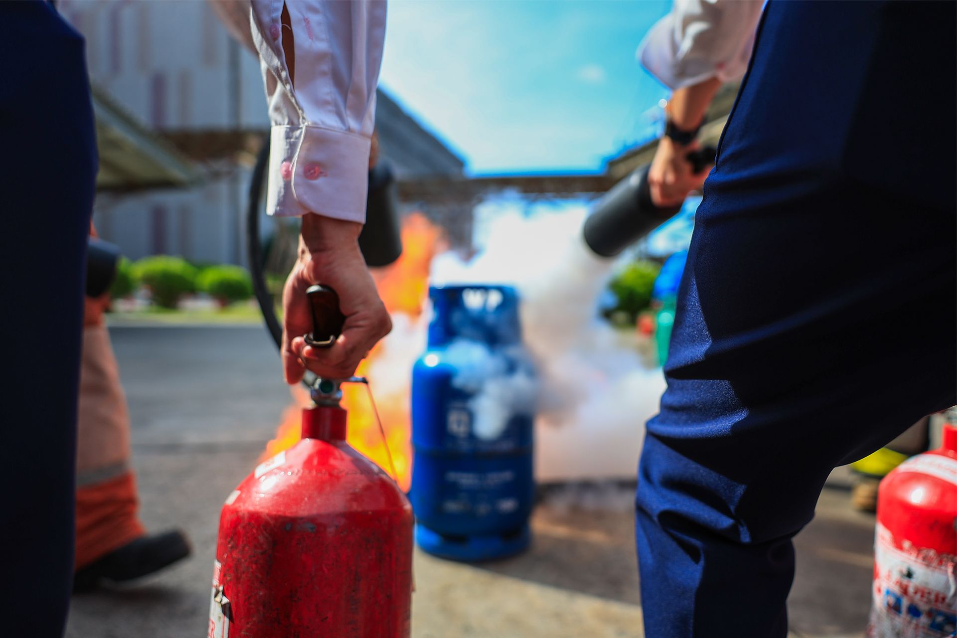People training to use fire extinguishers to put out a fire around a blue gas cylinder.