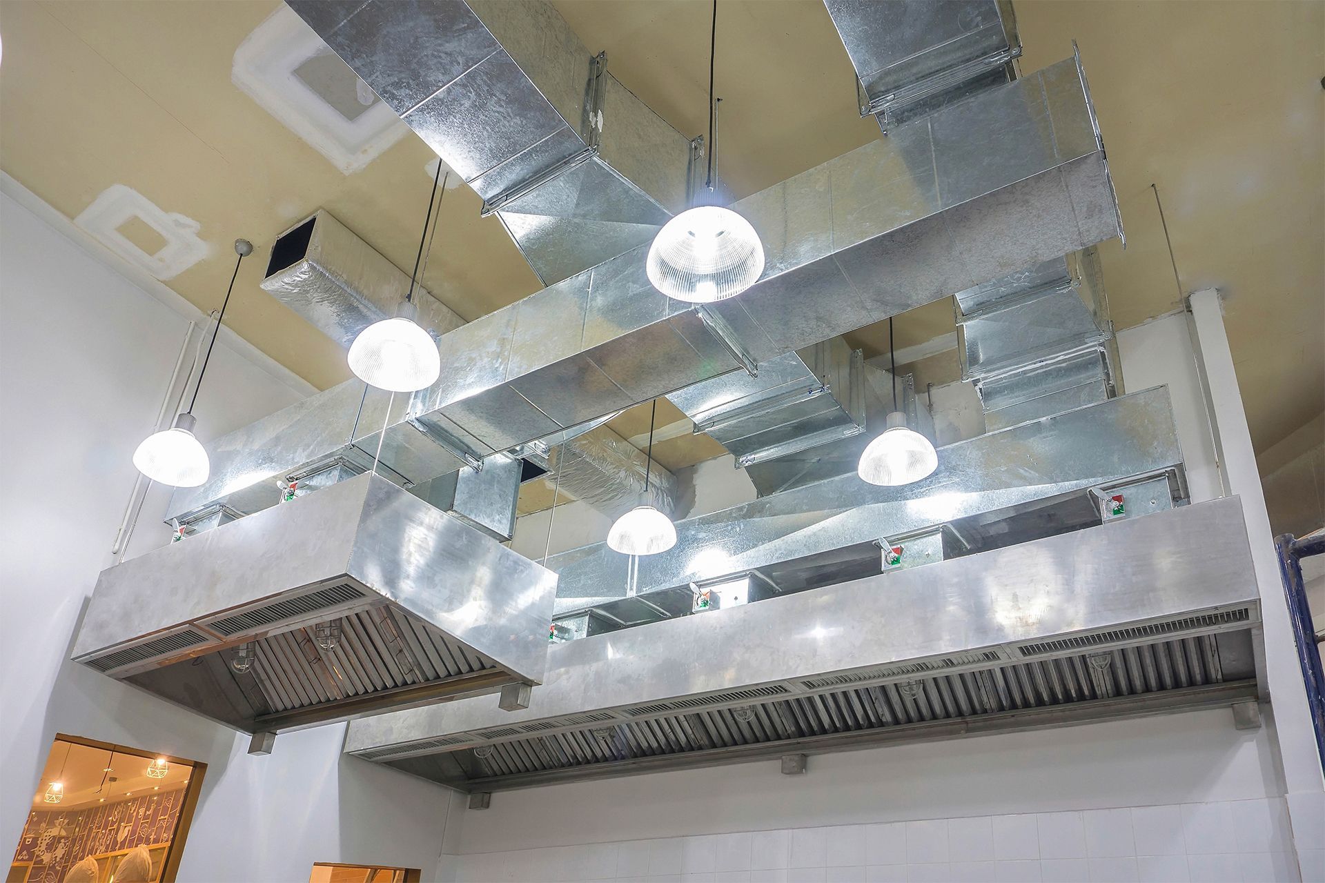 Kitchen ceiling with metal ventilation ducts, exhaust hoods, and hanging lights.