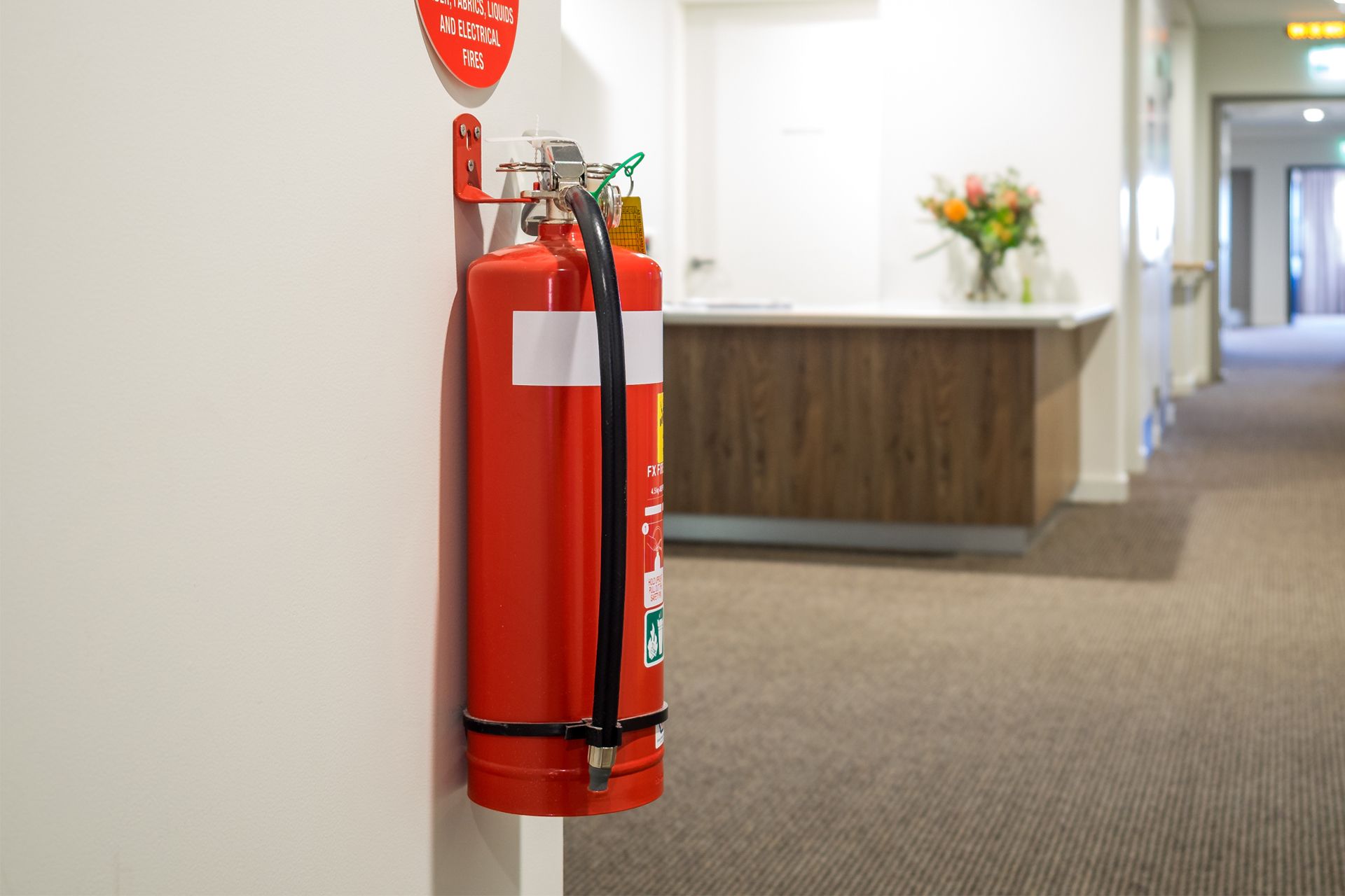 Red fire extinguisher mounted on a white wall in a hallway.