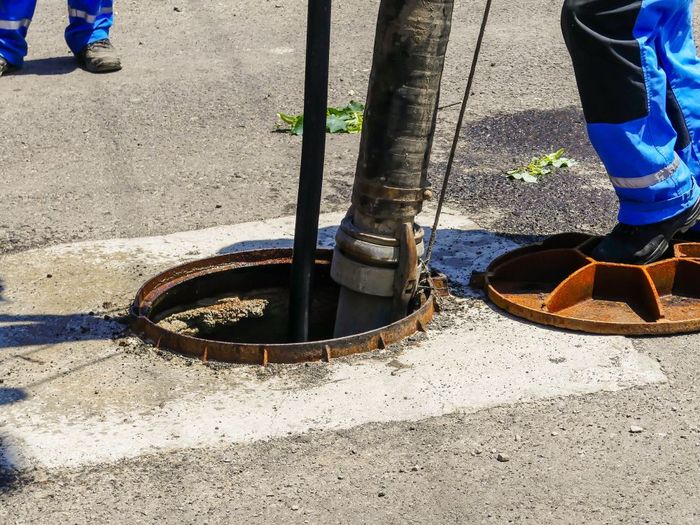 A man is cleaning a manhole cover with a hose.