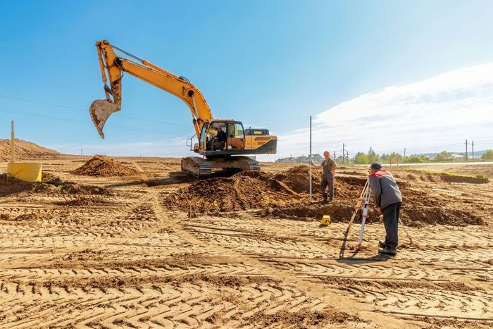 A construction site with a bulldozer and a man measuring the ground.