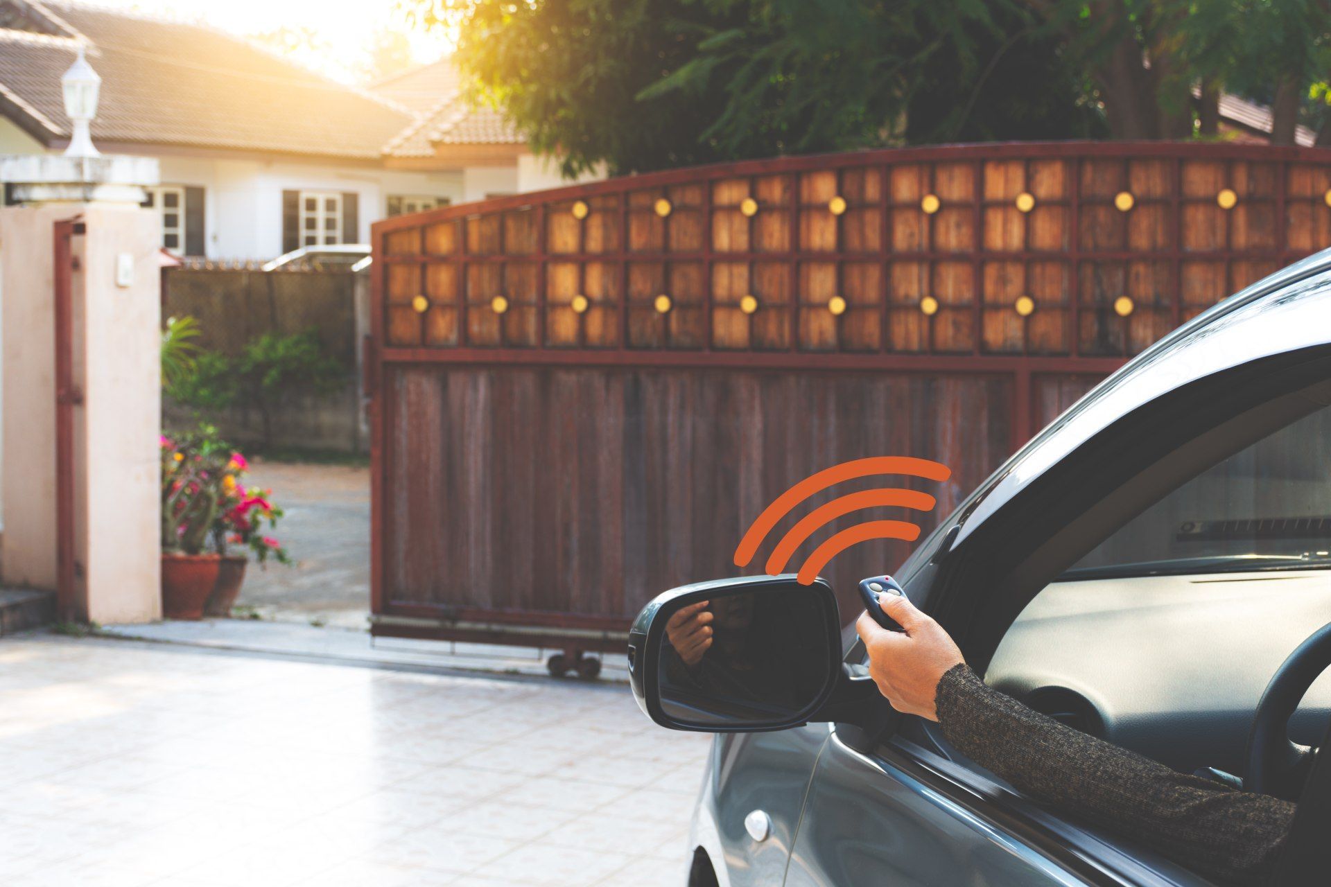 A person is driving a car and using a remote control to open a gate.