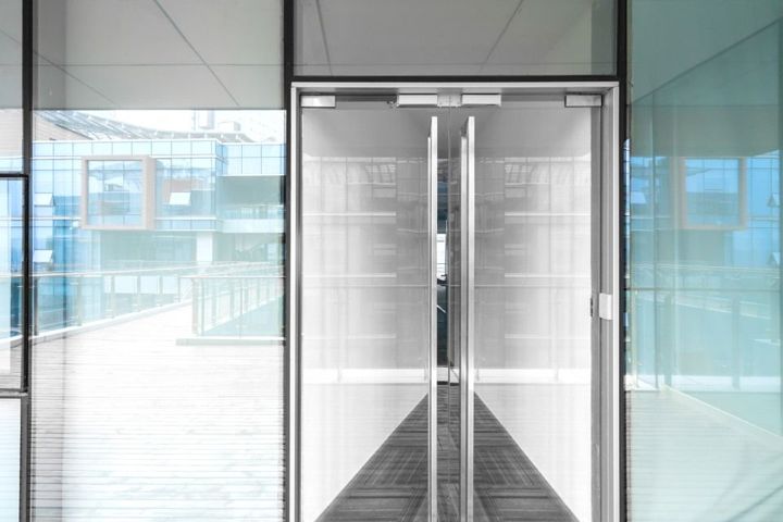 A hallway with a automatic glass door leading to a building.