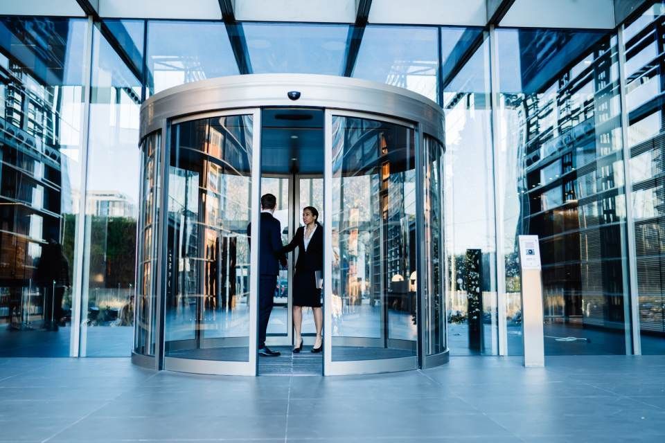 A man and a woman are standing in front of a revolving glass door.