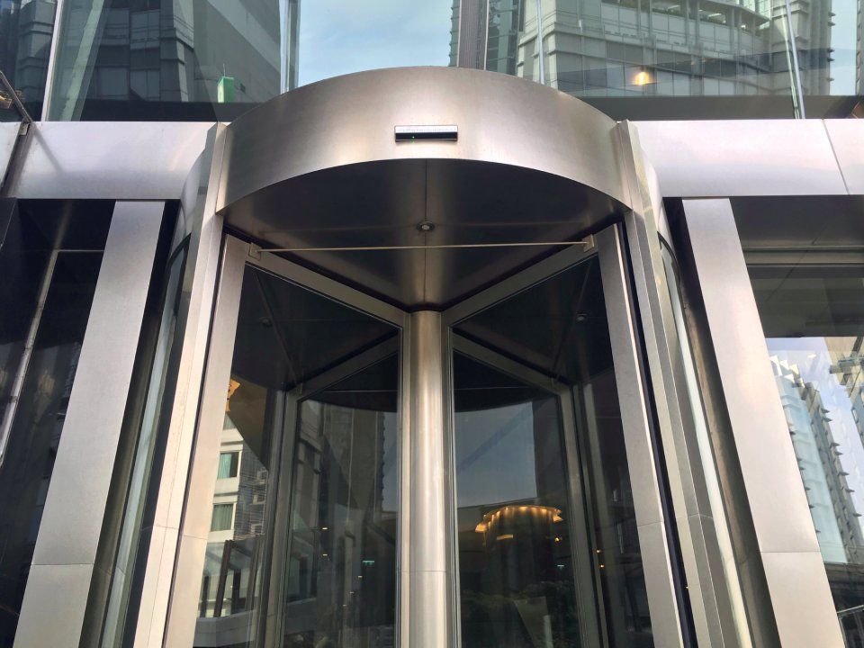 A stainless steel revolving door with a reflection of a building in the glass