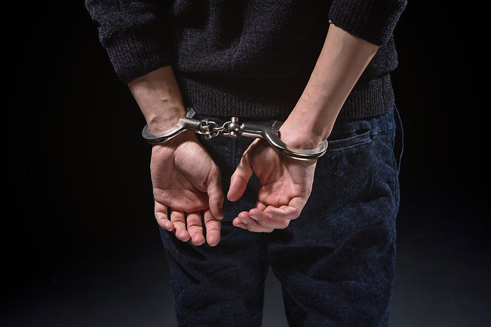 Personne menottée, les mains derrière le dos, vêtue d'un pull noir et d'un jean bleu.