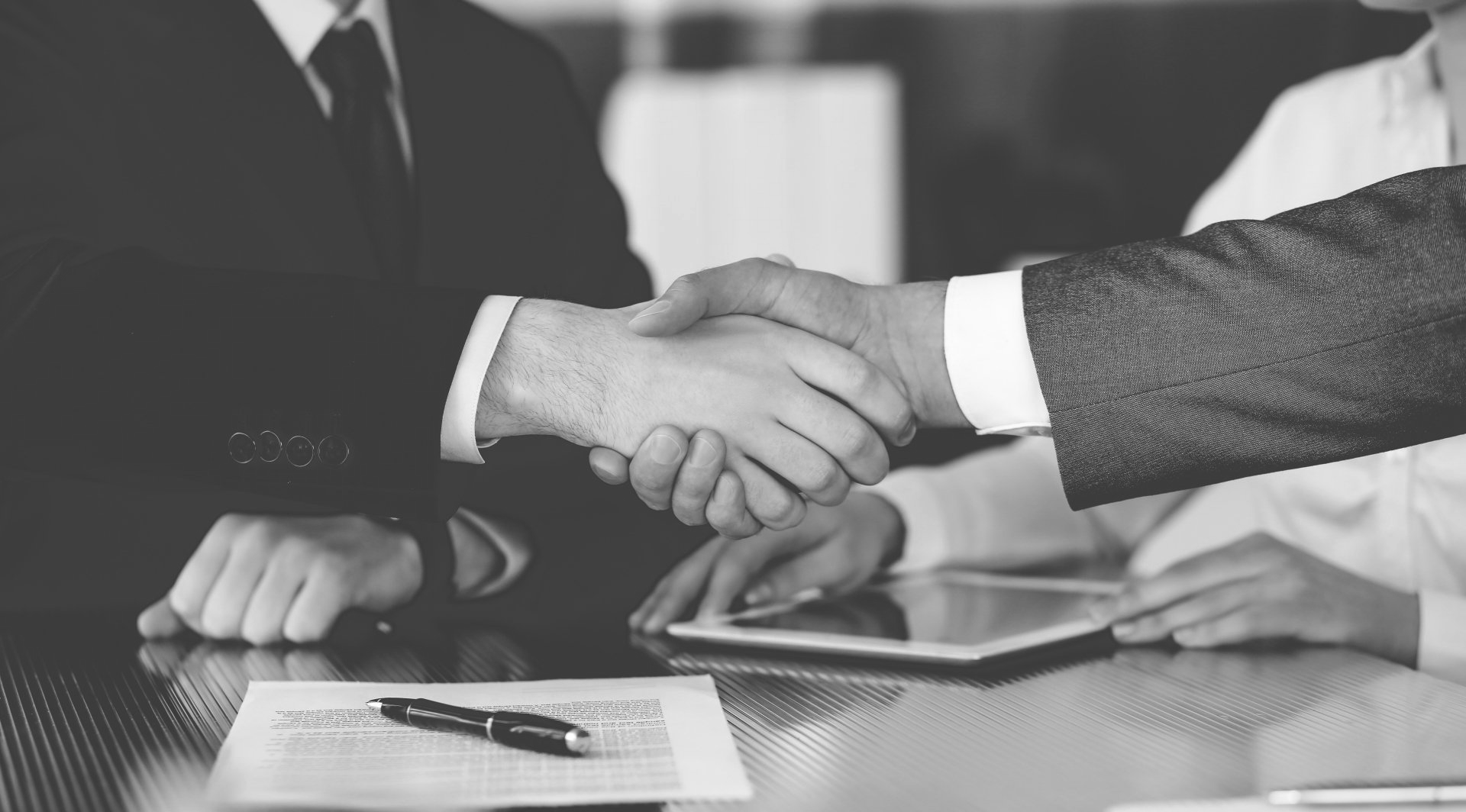 Deux hommes d'affaires se serrent la main au-dessus d'un contrat posé sur une table.