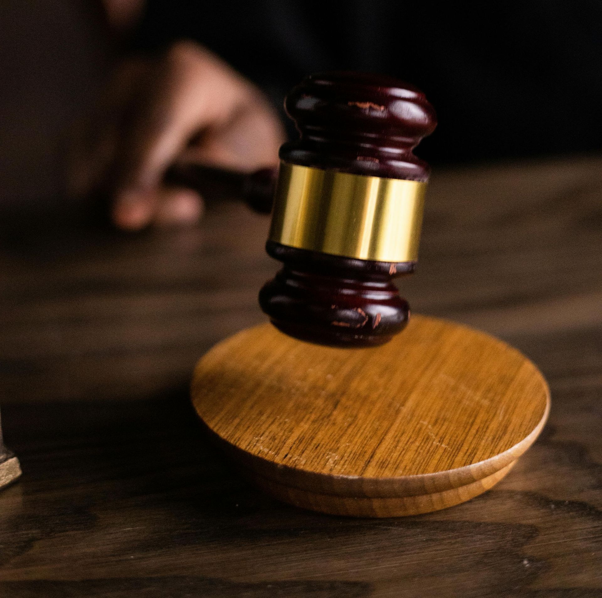 Un maillet frappe un bloc de bois sur une table en bois sombre. On aperçoit partiellement une main qui tient le maillet.