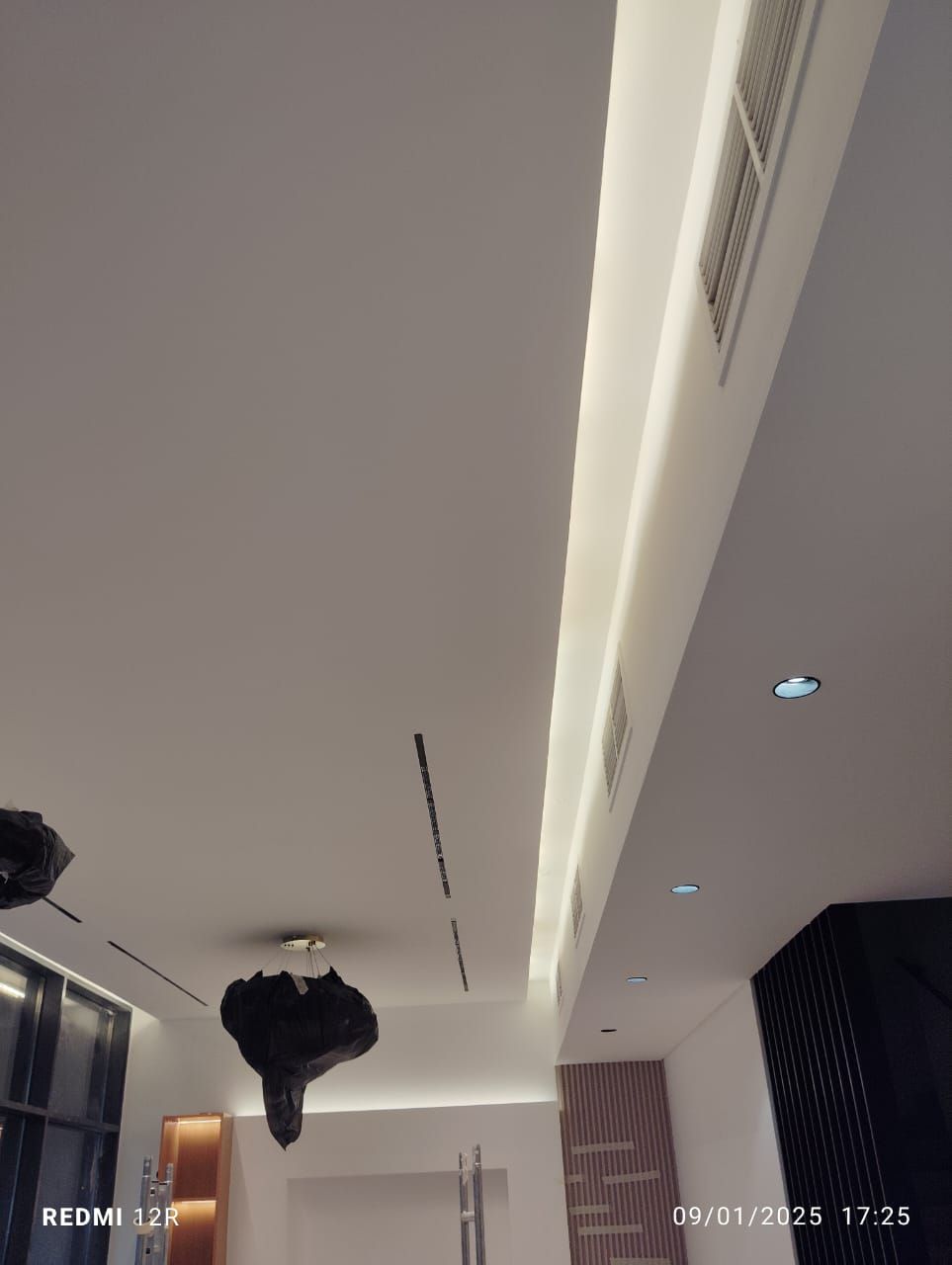 A modern white ceiling with recessed lighting and air vents.  A black abstract light fixture hangs below.