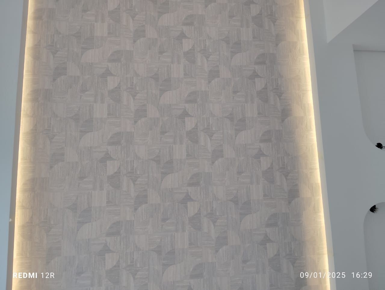 White wall with geometric pattern, illuminated by warm lighting.