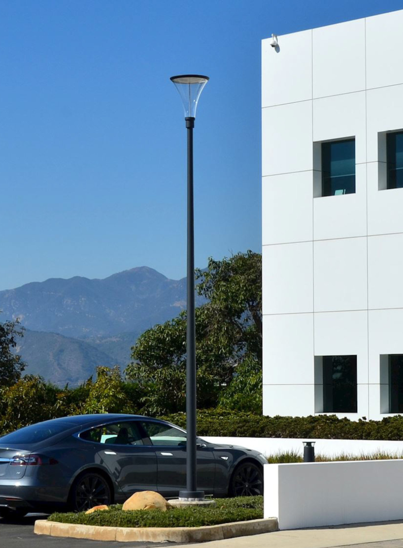 Solar-powered street light in front of a white building with a car and mountains in the background.