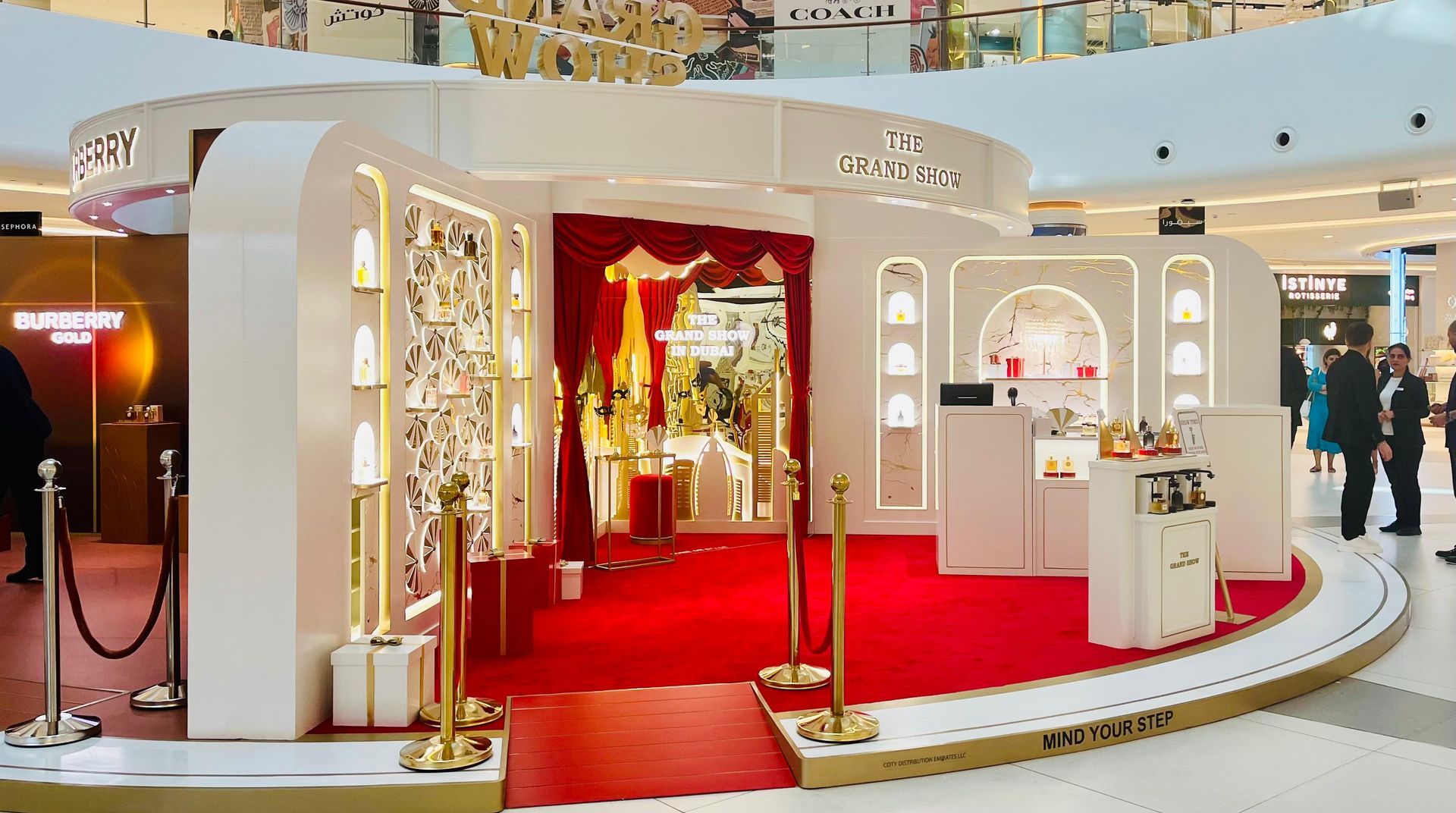 A luxury pop-up shop in a mall with red carpet and gold accents, showcasing products.