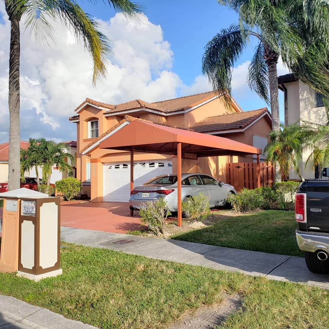 A car is parked under a canopy in front of a house